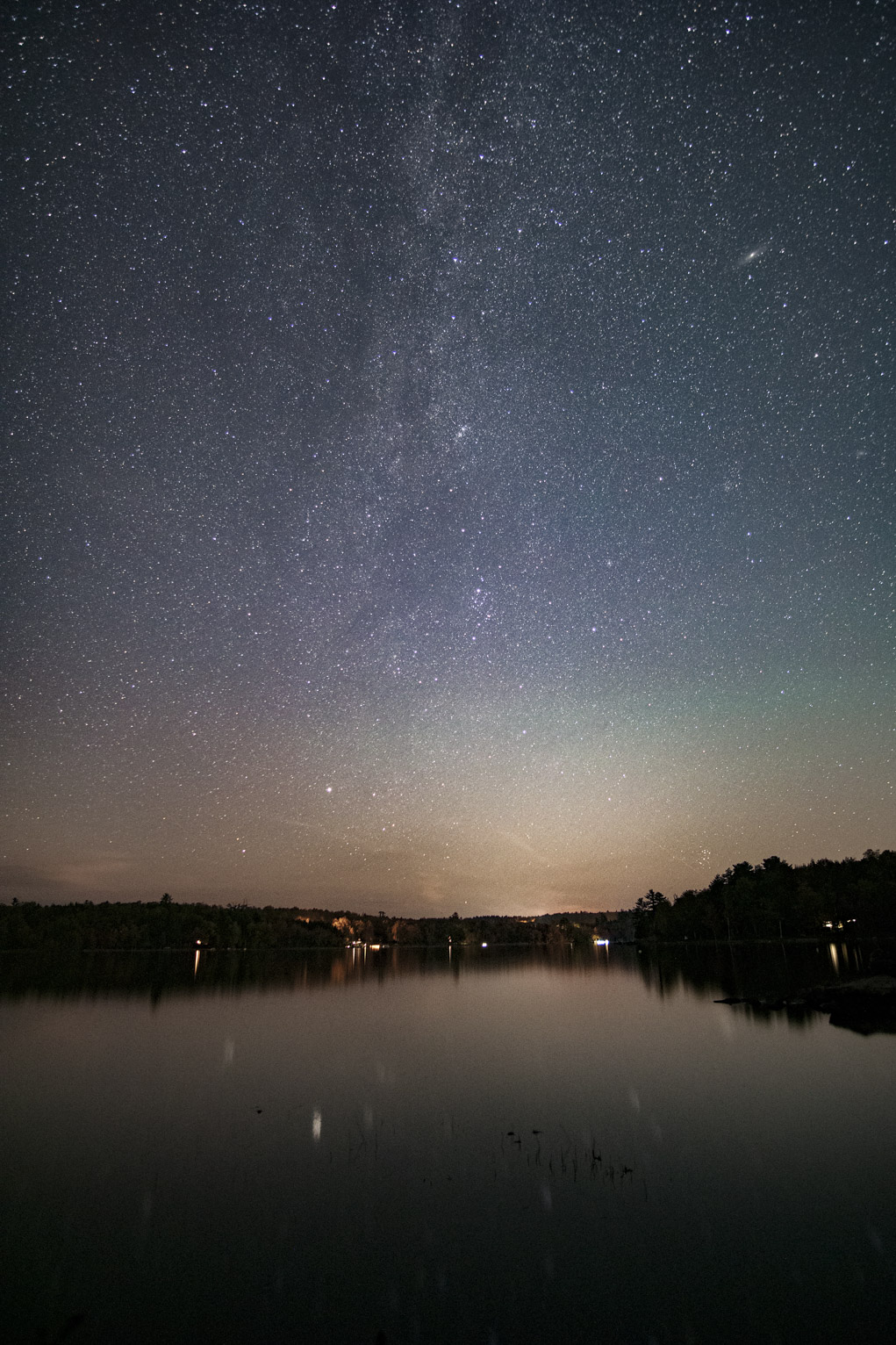 The milky way rises straight over the lake, the sky has hints of blue, green, purple, and orange